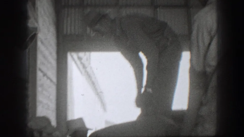 Backlit 1939 California frame with workers near large sacks inside a storage room, silhouetted by a bright doorway.