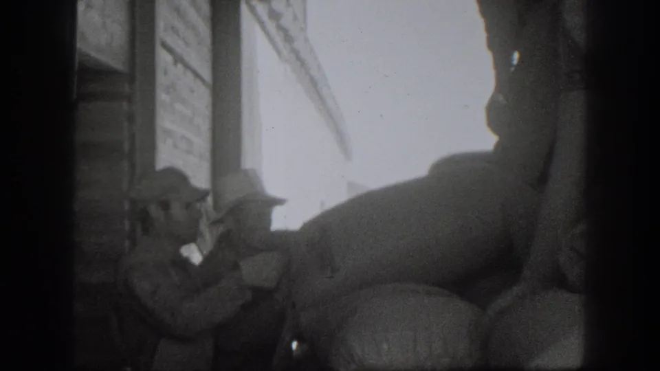 Men in hats appear to handle or secure a large sack near a bright doorway in 1939 California 8mm footage.