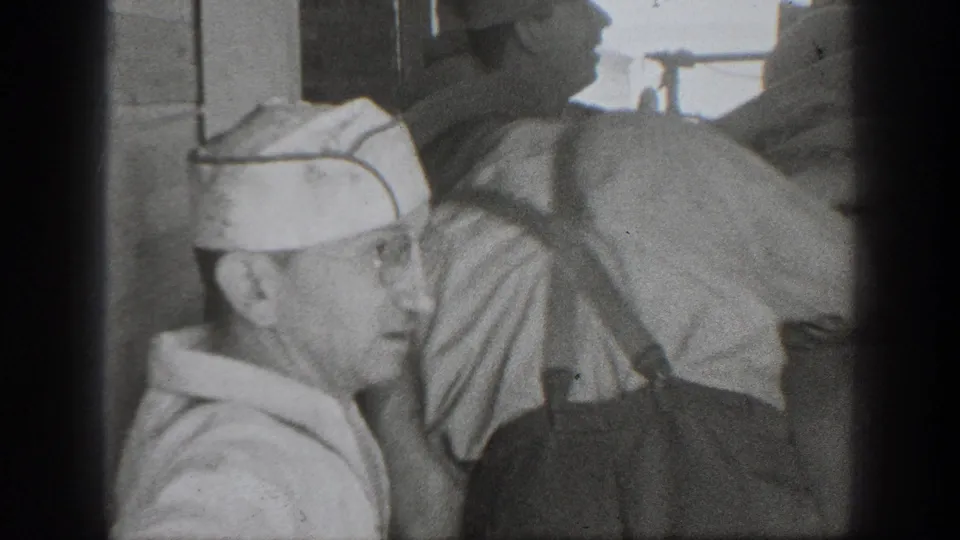 1939 California 8mm frame showing adult men in caps and workwear gathered around large sacks in a dim labor setting.