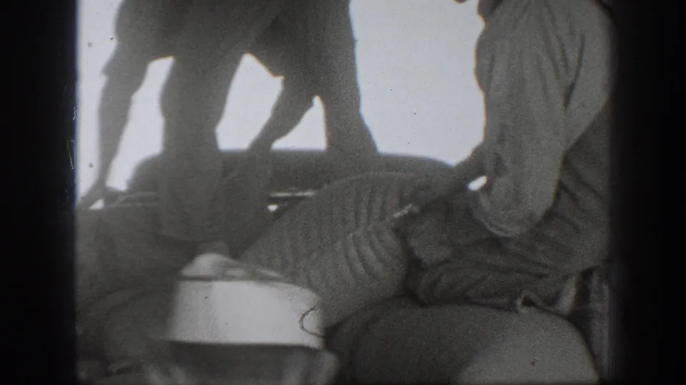 Black-and-white 8mm frame from 1939 California showing men bending and working around sacks in strong backlight.