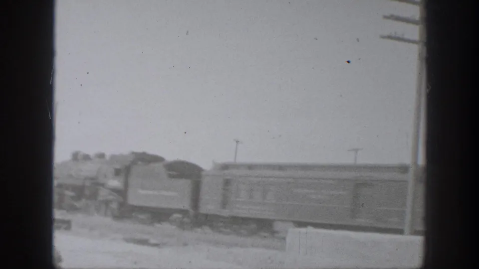 1939 California 8mm frame showing a steam locomotive pulling rail cars past open ground with utility poles in the distance.