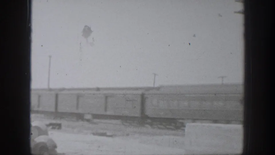 Black-and-white 8mm frame of passenger cars crossing a California trackside view, partly obscured by a dark vertical border.