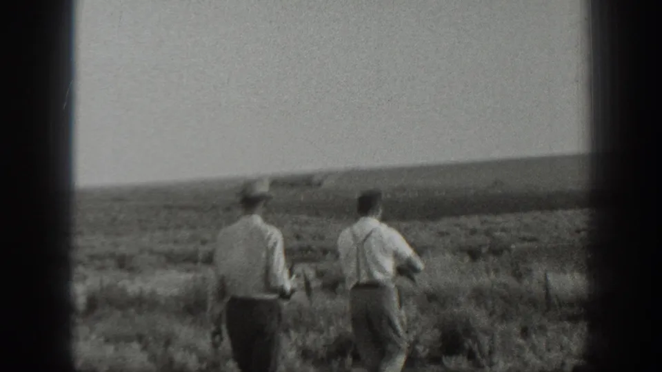 Two men walk across open rural land in the 1939 California home-movie footage, with one appearing to carry a rifle at his side.