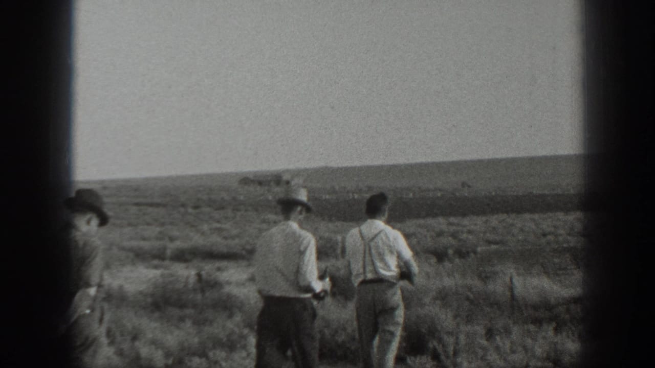 1939 California 8mm frame showing three adult men walking away through dry open ground, with hats, suspenders, and a rifle visible.