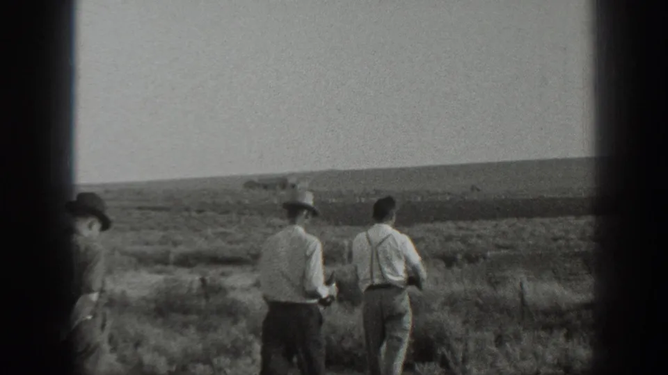 1939 California 8mm frame showing three adult men walking away through dry open ground, with hats, suspenders, and a rifle visible.