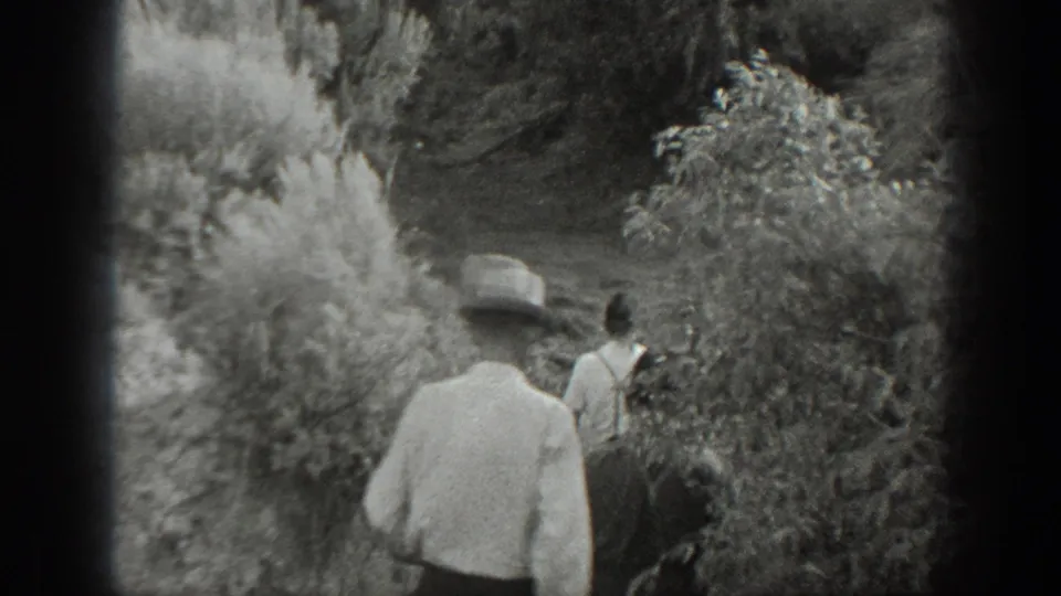 1939 California 8mm frame showing the men from behind as they move from open ground into dense brush and small trees.