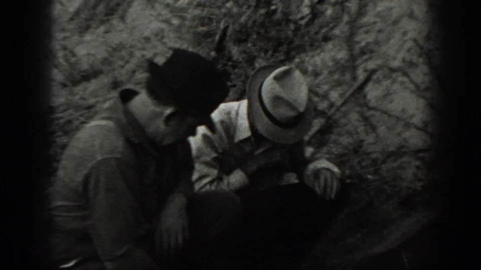 Two adult men in hats crouch near dense brush in 1939 California home-movie footage.