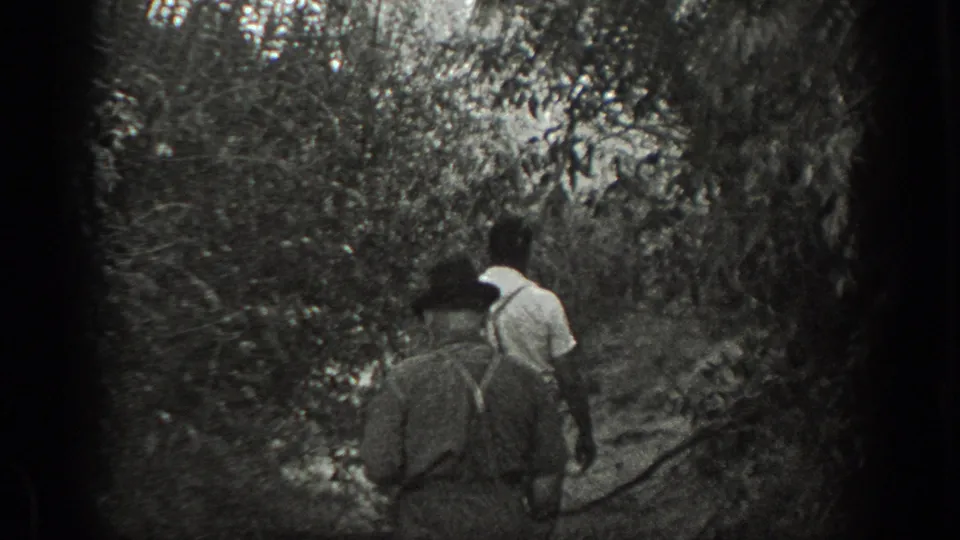 Two men, one in suspenders and one in a light shirt, walk away through a wooded California path.