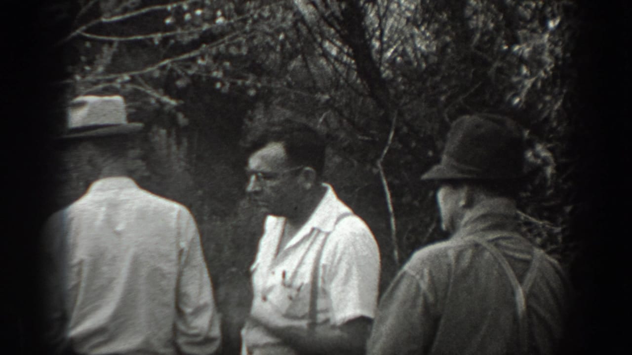 Several adult men stand together near trees and brush.