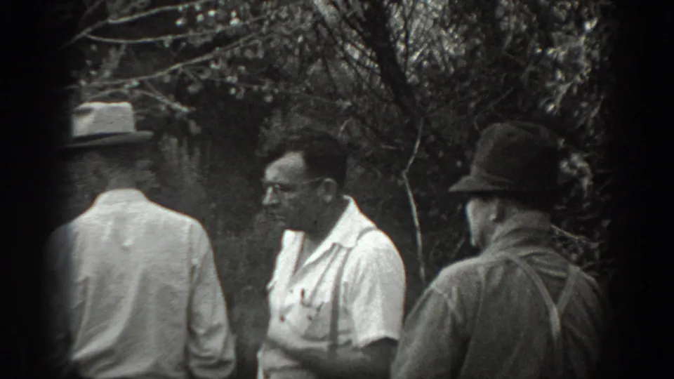 Adult men in hats and shirts gather in a wooded California setting, with one face partly visible in profile.