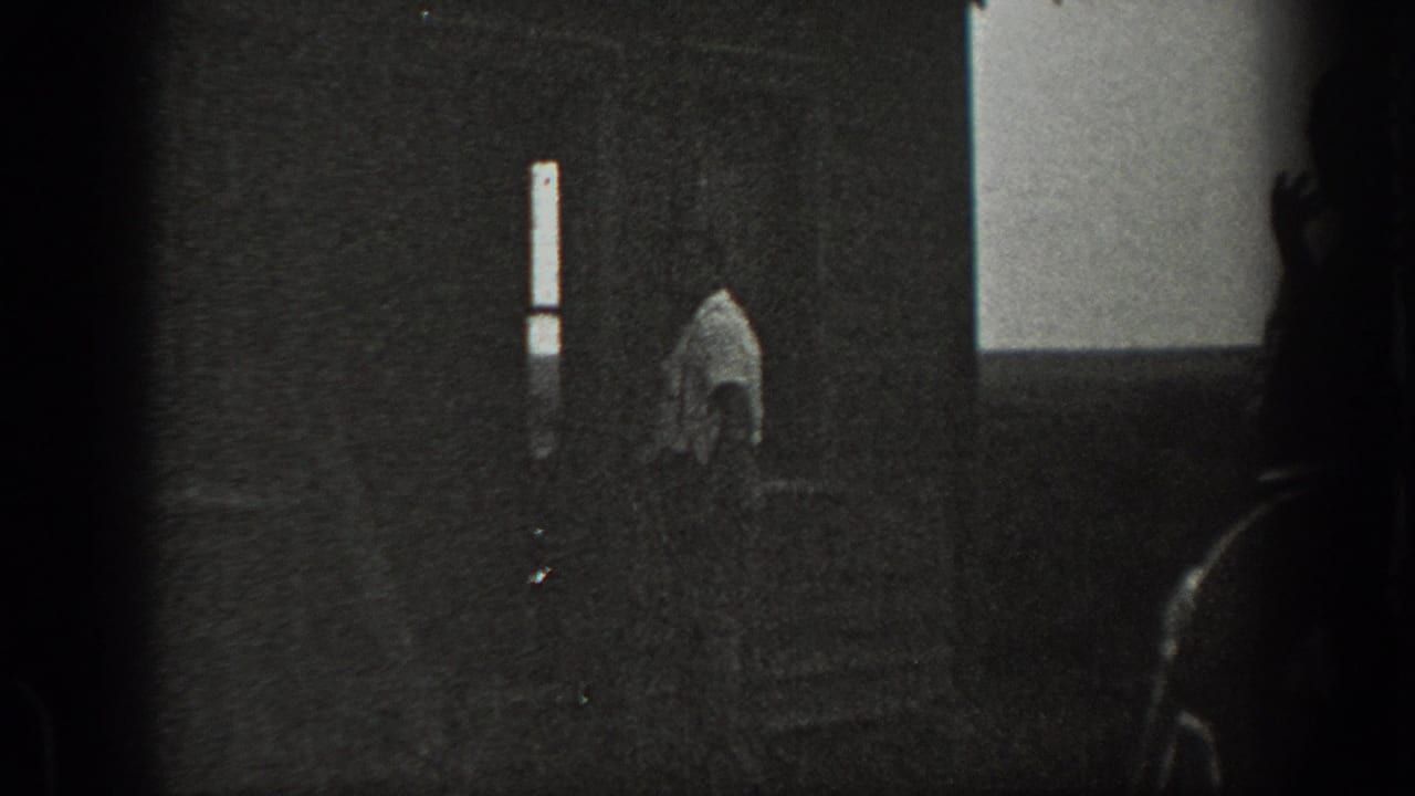 1939 California home-movie frame showing a dim interior, a man near a vertical window, and another shadowed figure partly visible at right.