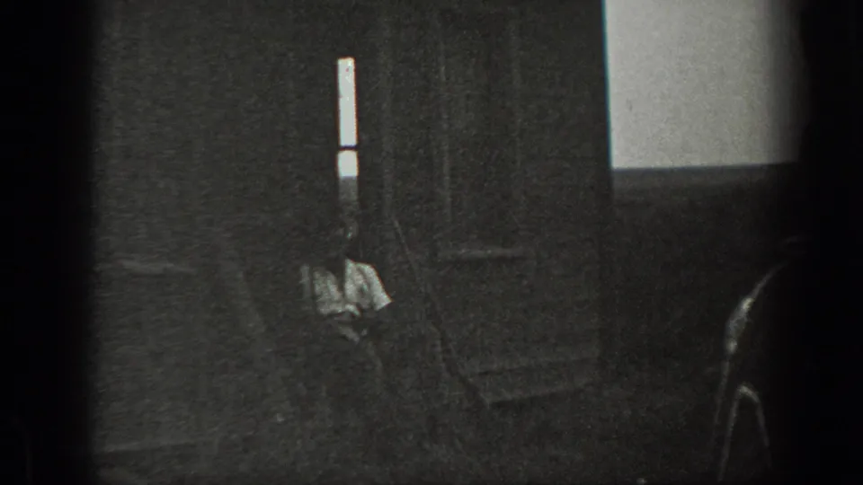 1939 California black-and-white frame with a man seated or crouched near the lower center of a shadowed private interior.