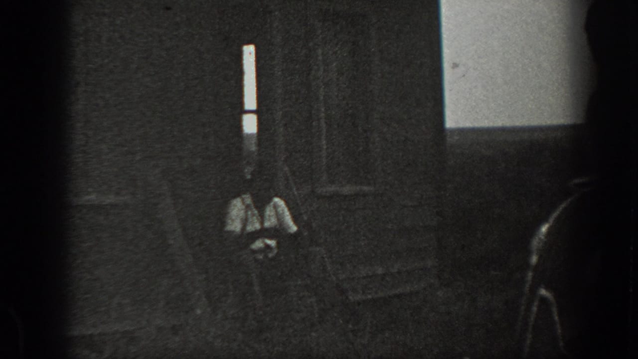 Dark, grainy 8mm frame from the supplied 1939 California clip, showing a shaded doorway or interior area with a faint seated figure shape.
