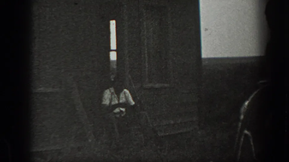 Dark, grainy 8mm frame from the supplied 1939 California clip, showing a shaded doorway or interior area with a faint seated figure shape.