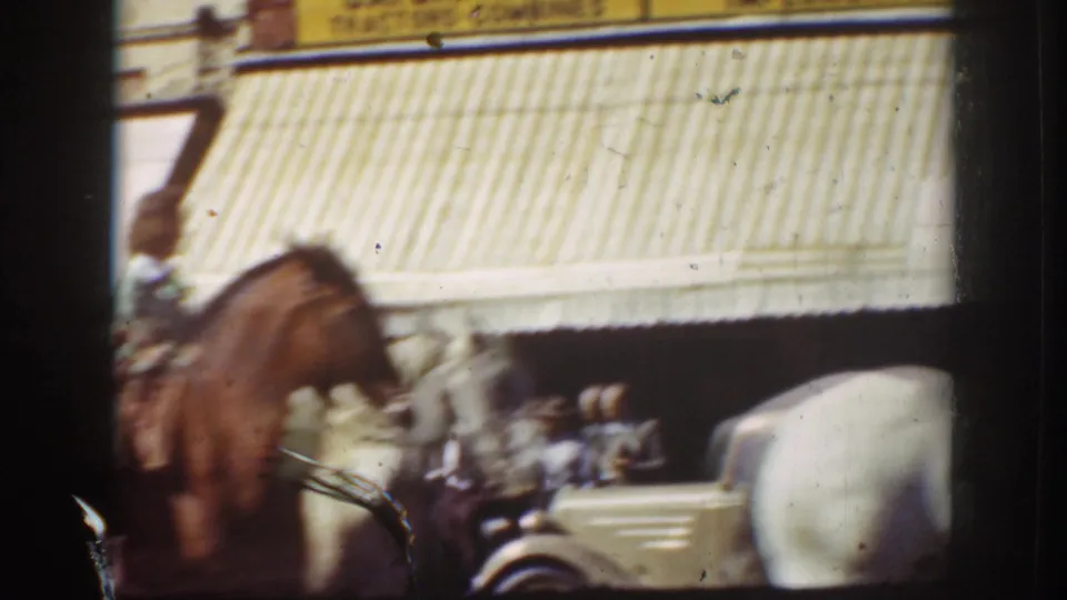 A rider on a brown horse passes storefront awnings and a visible John Deere sign in the supplied 1939 California street footage.