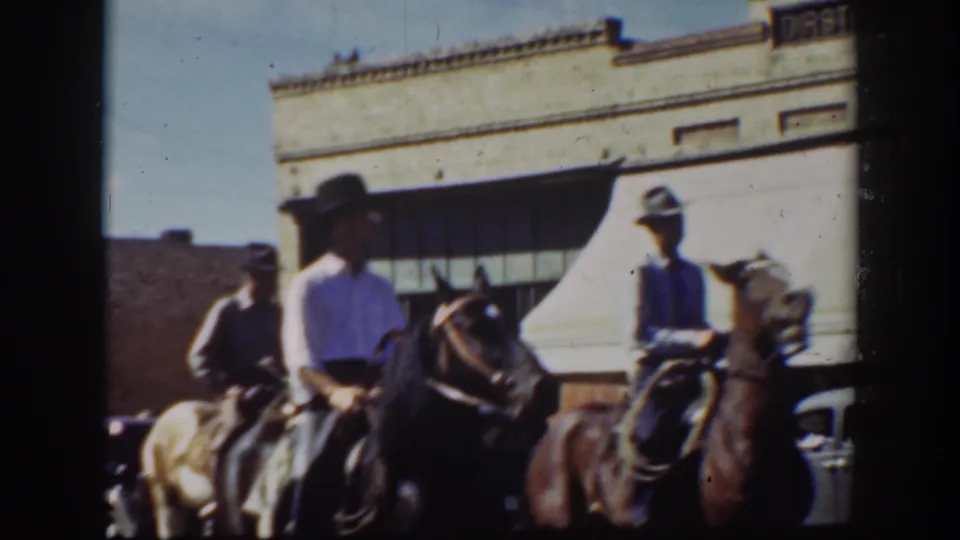 Horseback riders in hats appear near storefronts, awnings, and a parked car in the supplied 1939 California street scene.