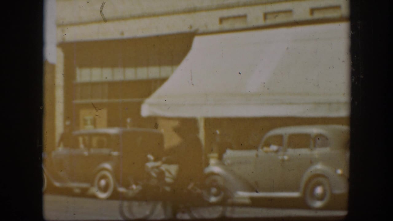 1939 California Main Street view with prewar automobiles, storefront awnings, and soft 8mm exposure.