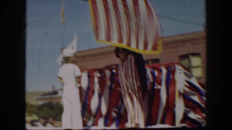 1939 California parade detail with a large U.S. flag, red-white-blue bunting, and a person in a white uniform or outfit.
