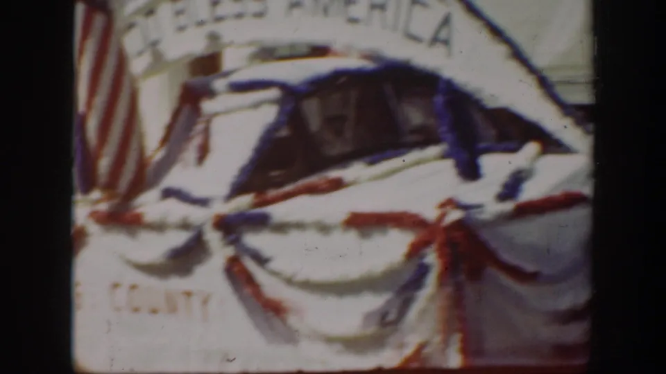 1939 California parade view with red-white-blue bunting on a vehicle or float and commercial storefront details behind it.