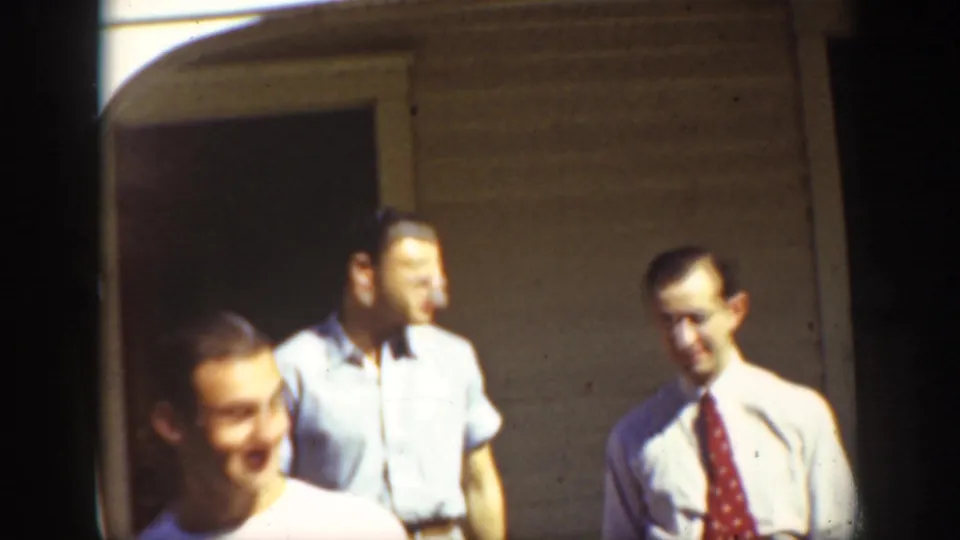 1939 California street frame showing several men in light shirts beside a building, including one wearing a tie.