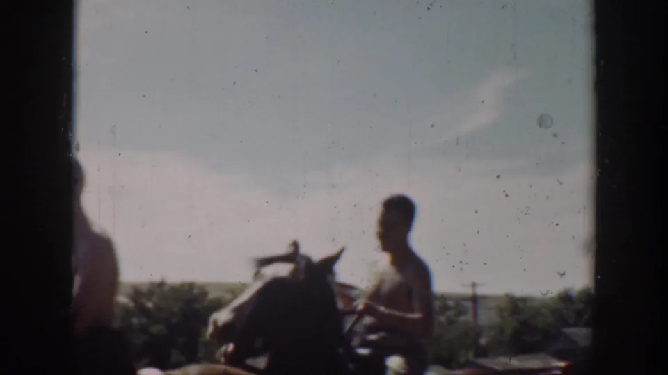 1939 California home-movie frame showing a shirtless man on horseback passing a dark doorway or window edge near open fields.