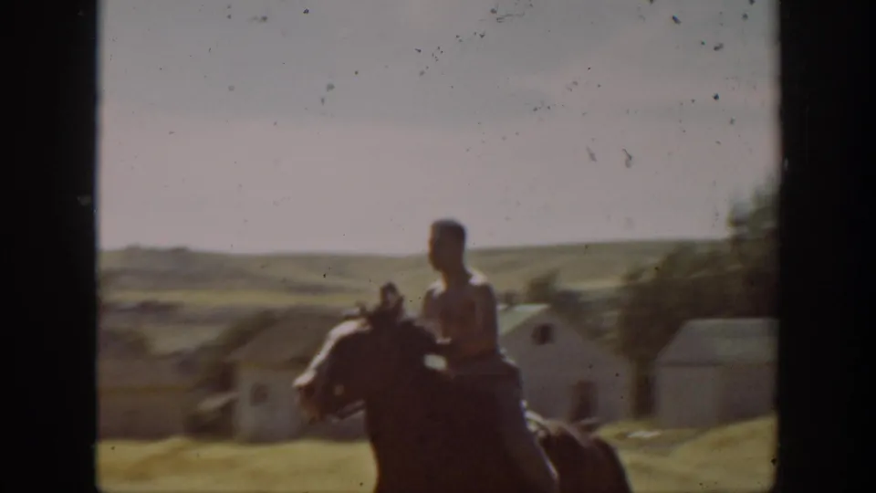 A shirtless rider on horseback passes near low farm buildings and trees in soft 1939 California 8mm footage.