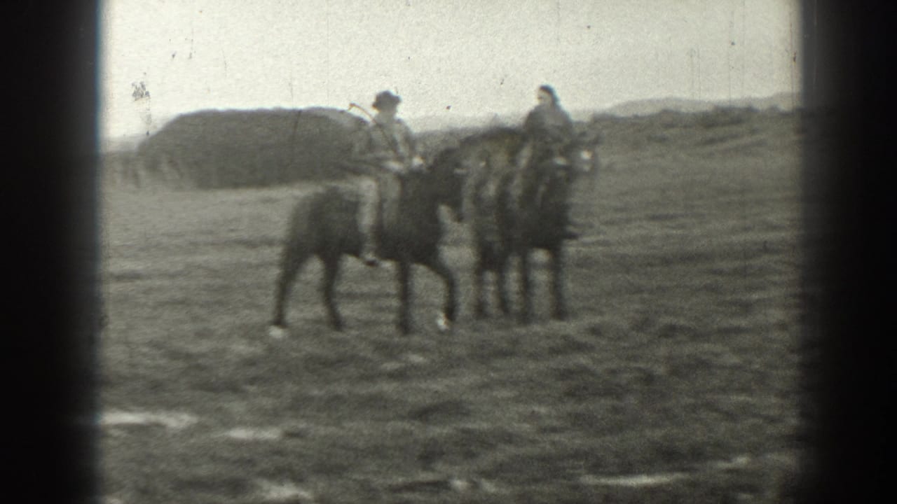 Two adults ride horses in a Montana ranch landscape, with soft 8mm edges and a low hill or mound in the background.