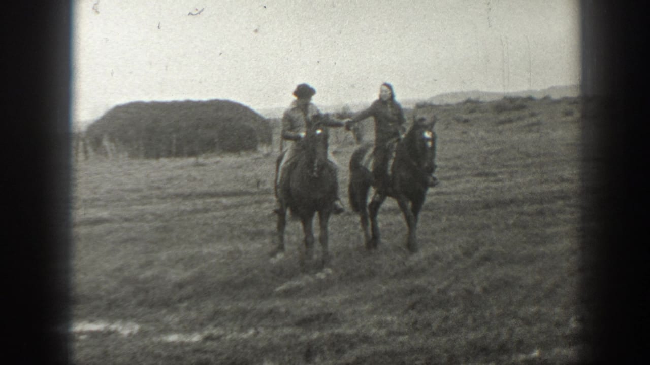 A couple rides side by side on horses while holding hands in a grassy valley.