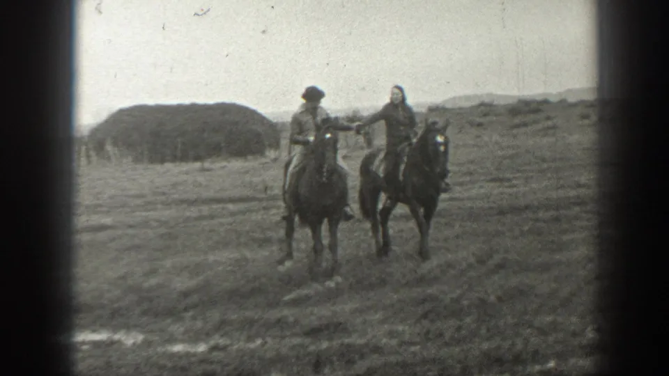 A man and woman appear to hold hands while riding horses across open Montana grassland in 1939 home-movie footage.