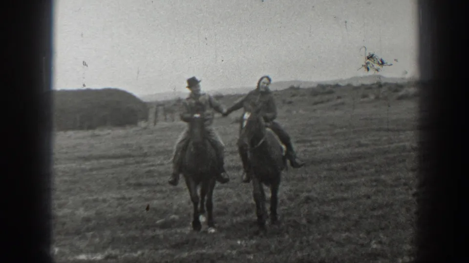 The couple faces the camera on horseback in 1939 Montana footage, holding hands against grassland and distant hills.