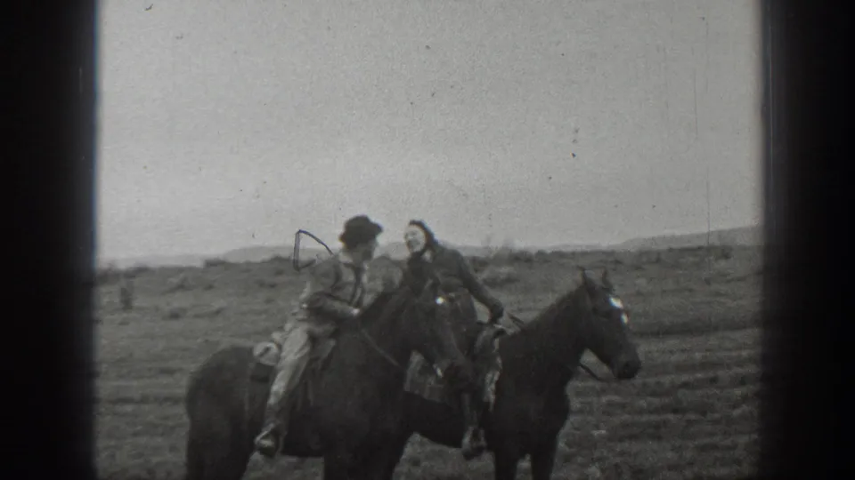 In the supplied 1939 Montana 8mm home-movie footage, a man in a hat and a woman in a long coat sit on separate horses and lean together on open plains.