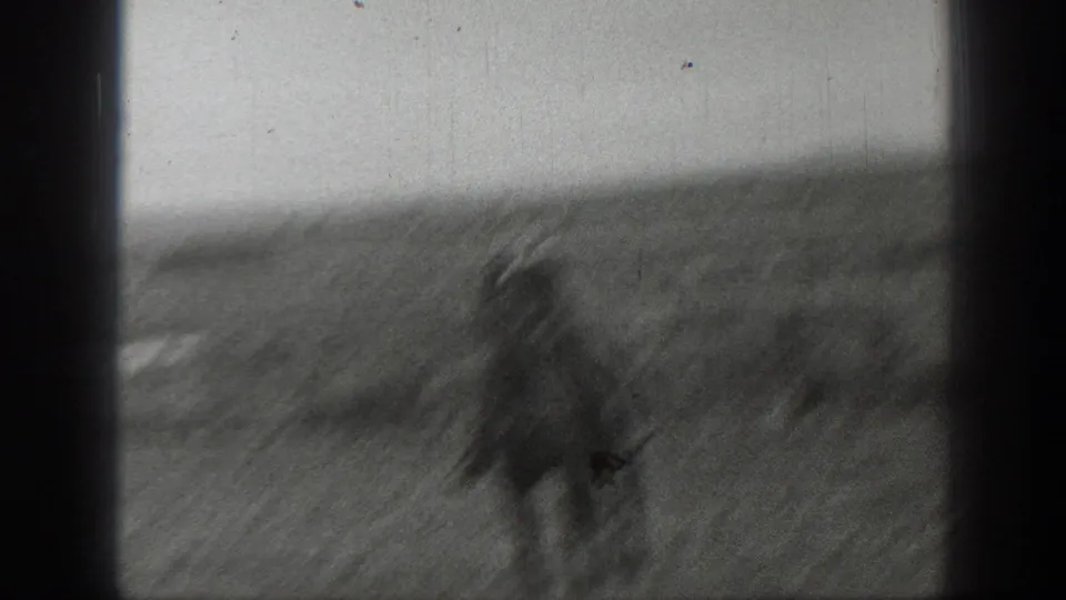 A blurred rider and horse move through the grassy Montana field, with motion blur and soft focus emphasizing the handheld 8mm home-movie character.