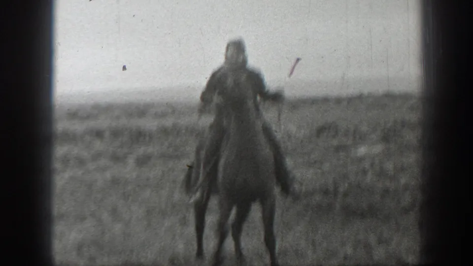 A mounted figure faces toward the camera on a horse in the open Montana field, with the background softened by grain, scratches, and exposure haze.