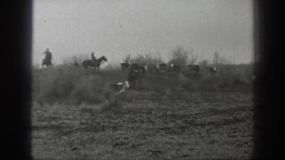 In the supplied 1939 Montana context, distant riders on horseback herd cattle across sparse open ground.