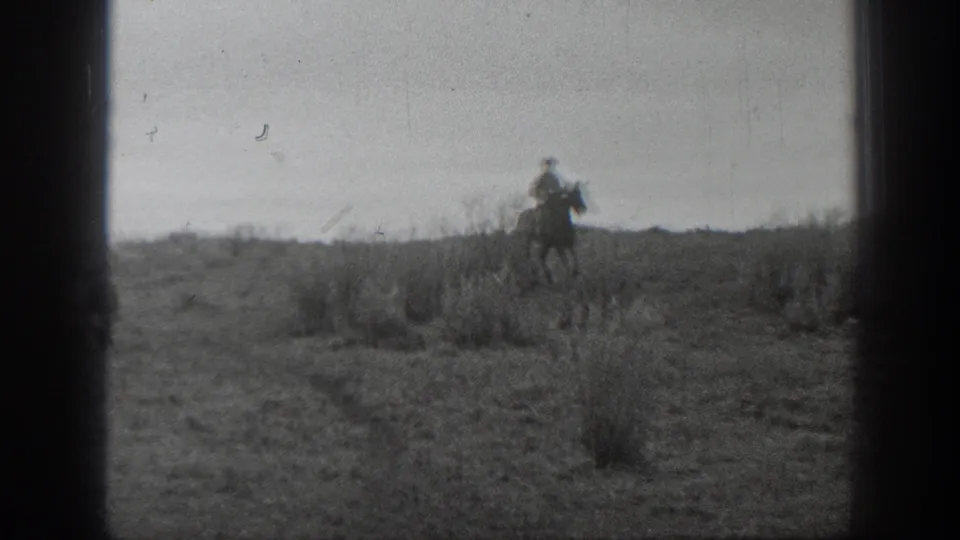 1939 Montana 8mm frame with a horseback rider crossing brushy prairie, framed by dark film edges and visible scratches.