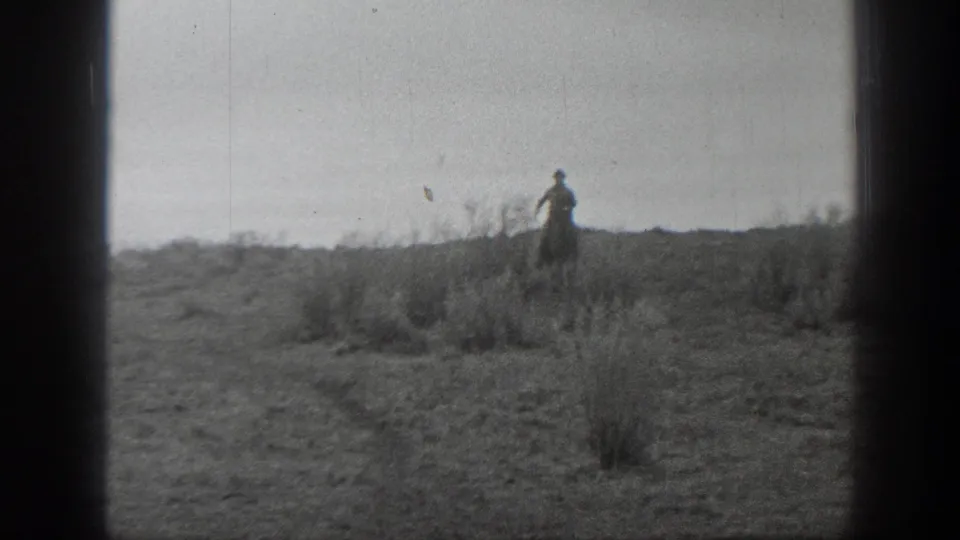 A distant cowboy figure appears on open Montana prairie in black-and-white 8mm footage, with low scrub and dark frame borders.