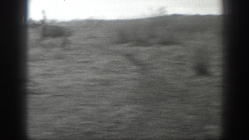 Open prairie terrain in the Montana ranch sequence, with low brush, soft focus, and black 8mm frame edges.