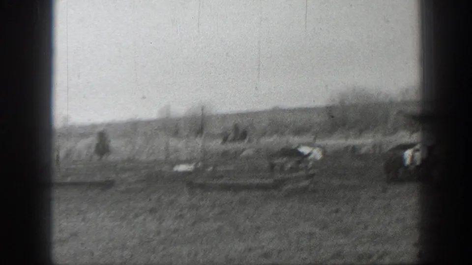 Black-and-white 1939 Montana home-movie frame showing cattle scattered across a rural field near low farm structures.