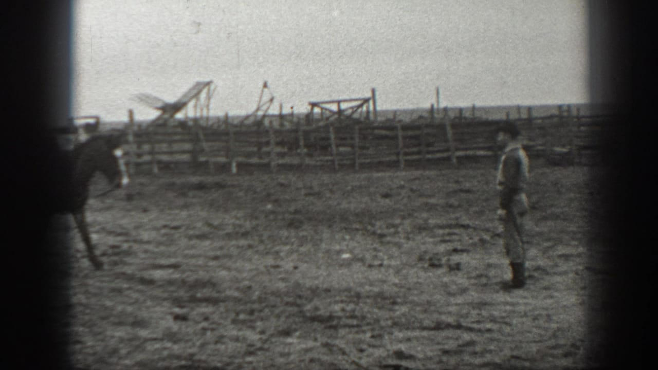 In 1939 Montana home-movie footage, a saddled horse moves across a fenced corral toward a standing man.