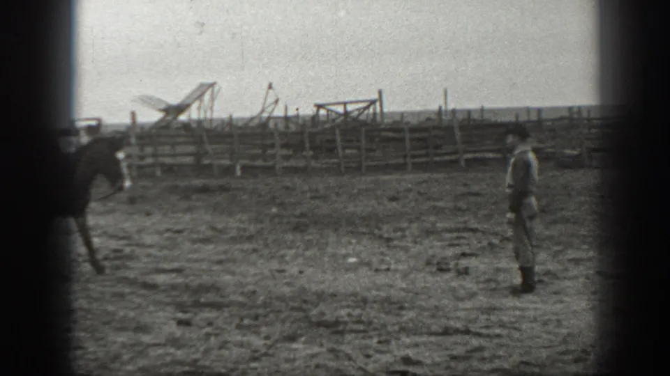 In 1939 Montana home-movie footage, a saddled horse moves across a fenced corral toward a standing man.