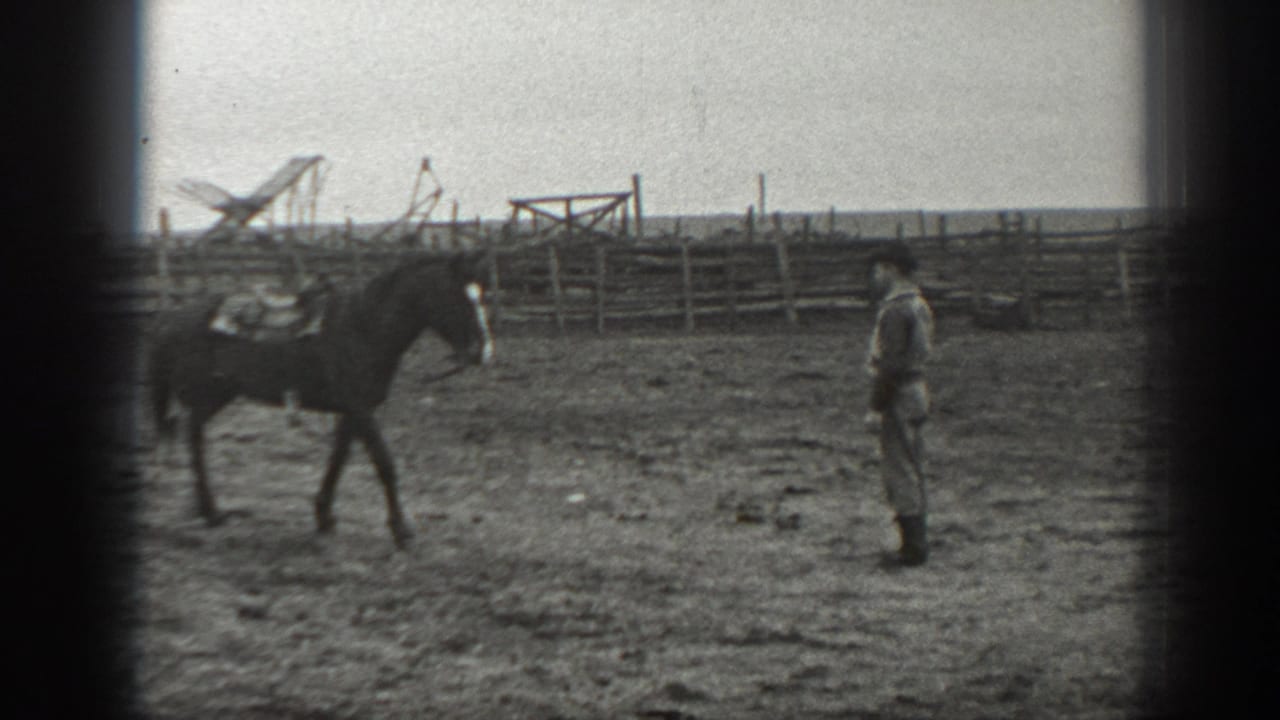 A saddled horse crosses the corral toward a man in period attire, with wooden fencing behind them.