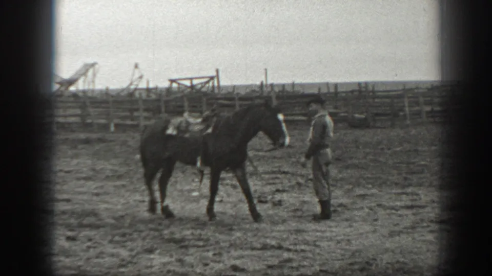 The saddled horse stands close to the man in the Montana corral as he faces its neck and head area.