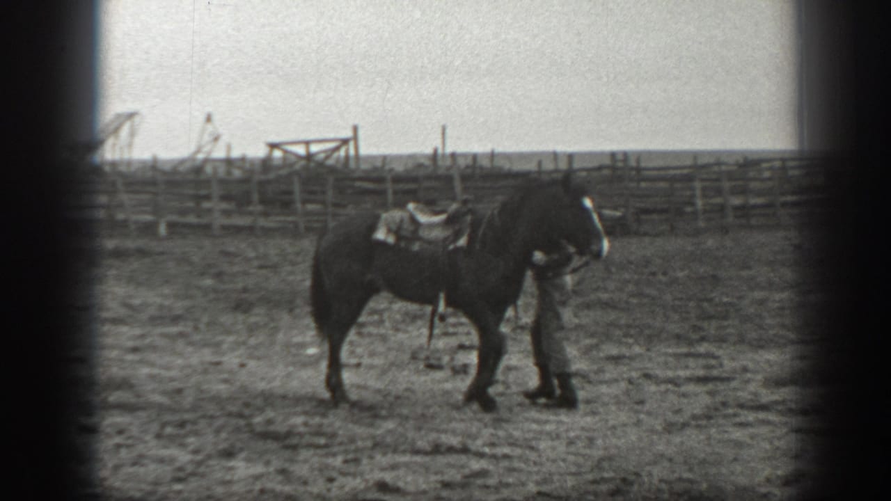 In 1939 Montana ranch footage, a man in work clothes stands close to a saddled dark horse near rail fencing.