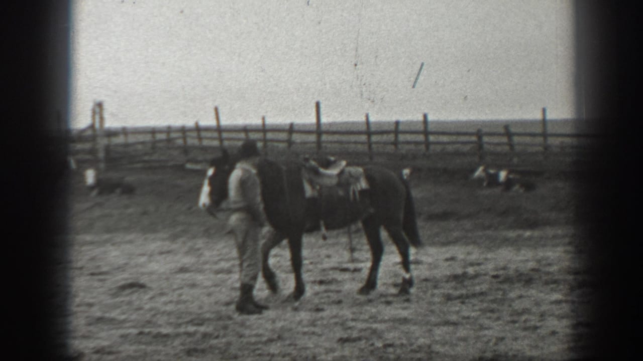 In 1939 Montana home-movie footage, a man leads a saddled horse through a dusty fenced yard with open land behind.