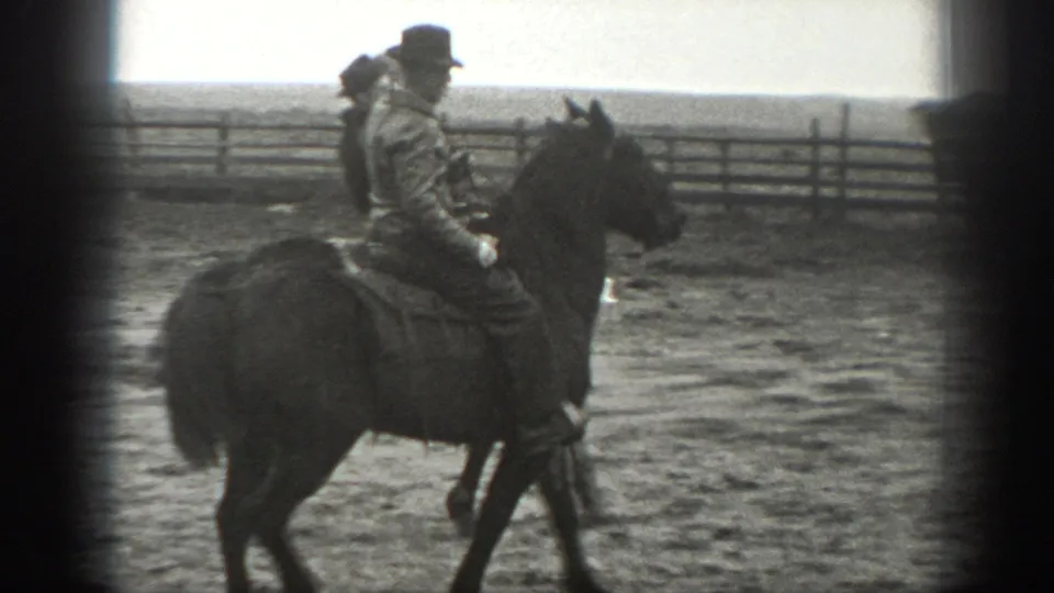 1939 Montana 8mm frame showing a side view of a man on horseback crossing a dusty wooden corral.