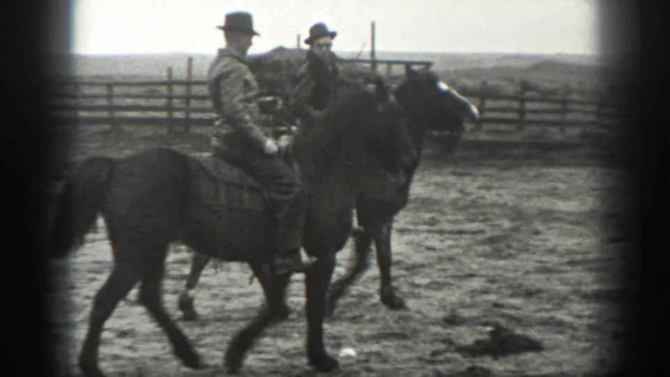 1939 Montana 8mm frame showing two men on horseback inside a wooden corral, with one horse partly turned toward the camera.