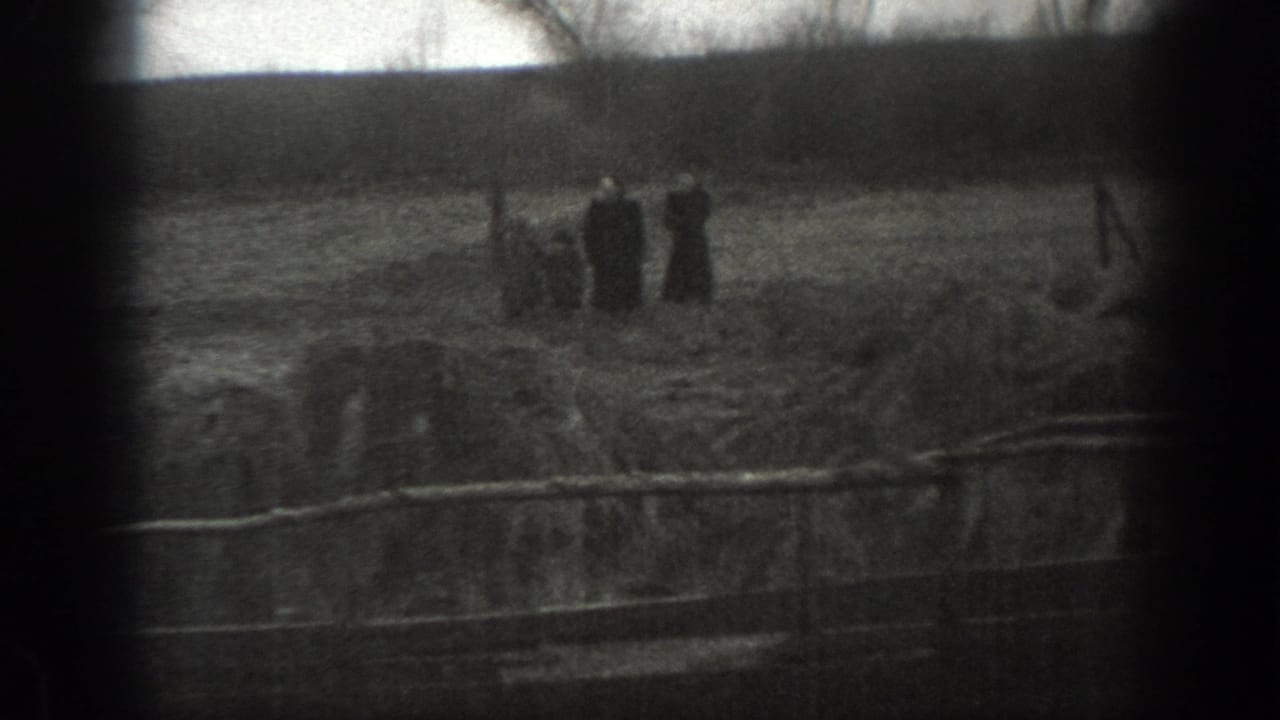1939 Montana home-movie frame showing distant farm figures near a ditch or fence line in an open field.