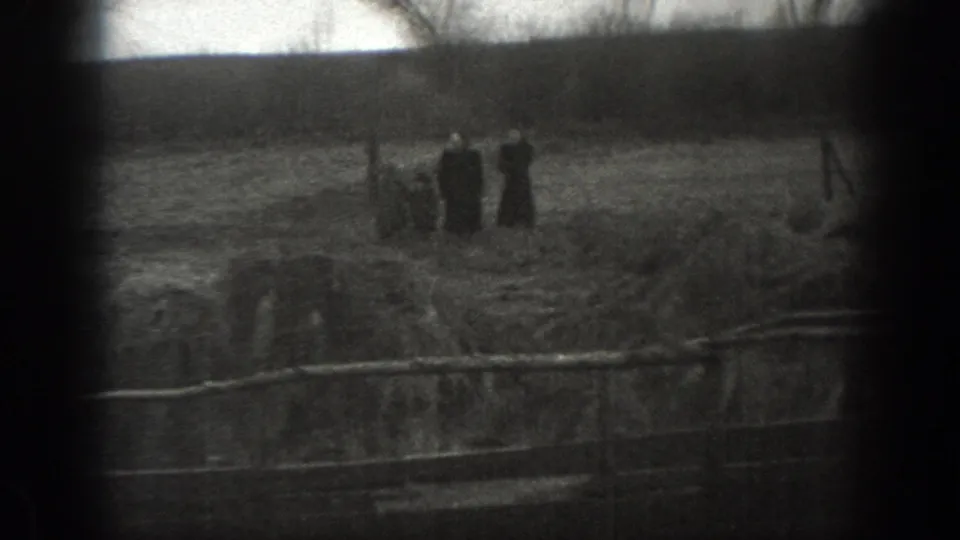 1939 Montana home-movie frame showing distant farm figures near a ditch or fence line in an open field.