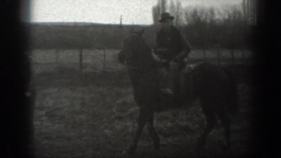 1939 Montana home-movie frame of a hat-wearing rider on horseback beside field fencing and bare trees.