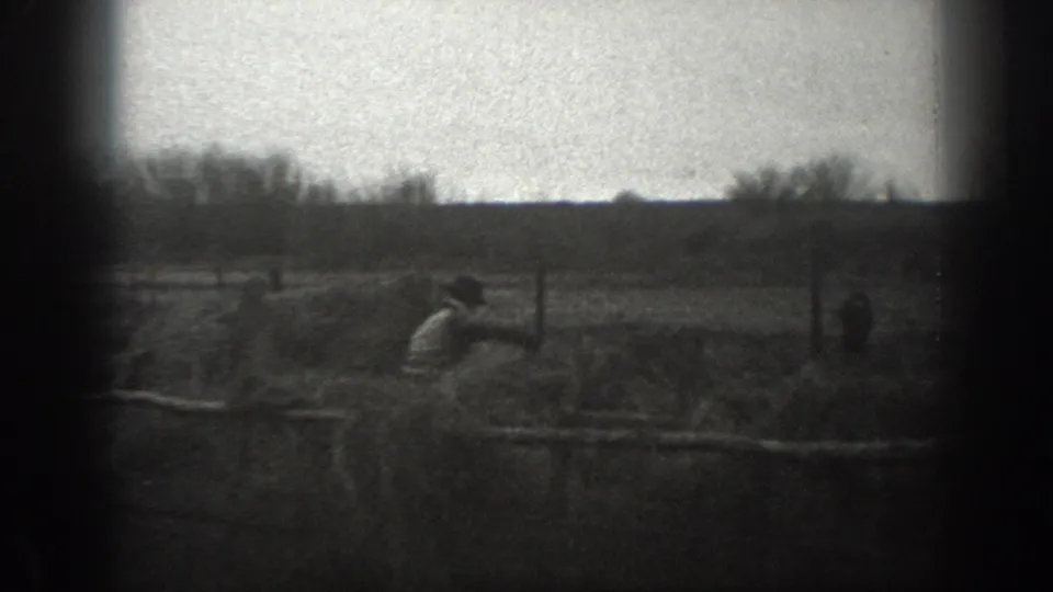 1939 Montana farm scene with distant figures, small animals, rough wooden fencing, and open pasture visible through soft 8mm grain.